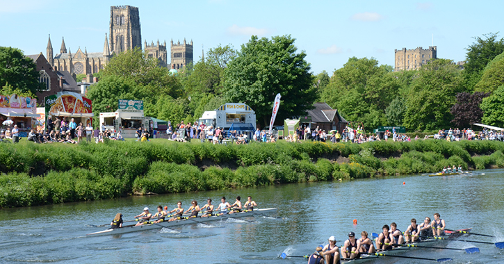people standing on riverbanks in Durham City watching the Durham Regatta with Durham Cathedral in the background